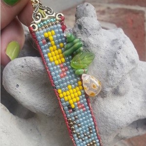 A bracelet of beadwork, depicts yellow birds and the word 'kweh' on a blue background.